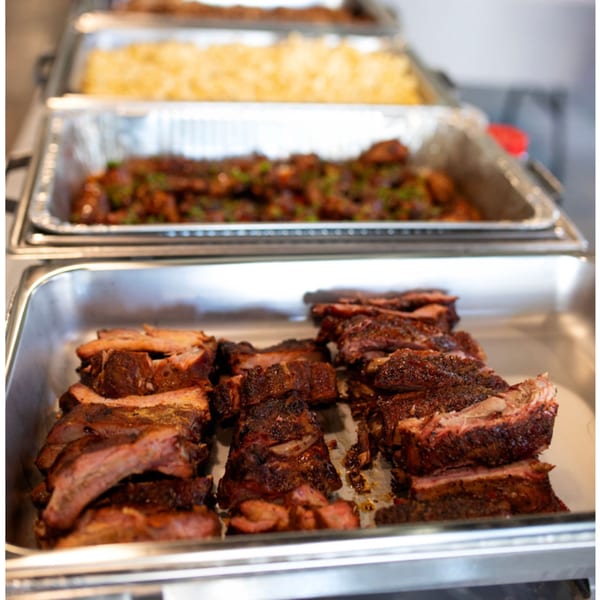Close-up of buffet-style trays filled with barbecue ribs, mac and cheese, and another dish.