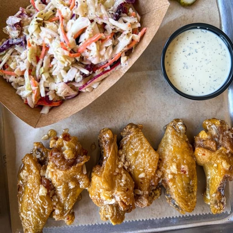 Five glazed chicken wings with a side of coleslaw and ranch dressing on a metal tray.