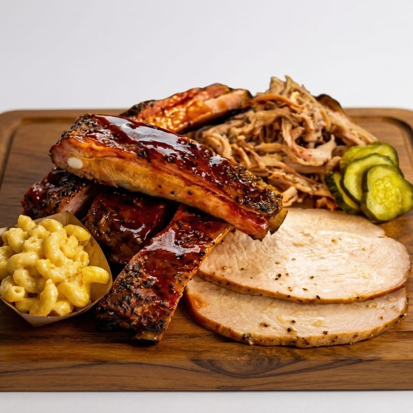 A wooden board piled with BBQ ribs, pulled pork, sliced turkey, macaroni and cheese, and pickles.